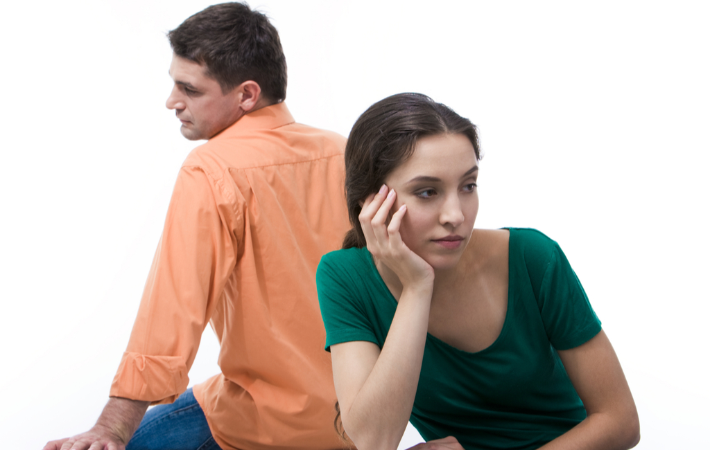 Man and woman with their backs against each other both looking pensive, woman has hand on cheek looking a little frustrated